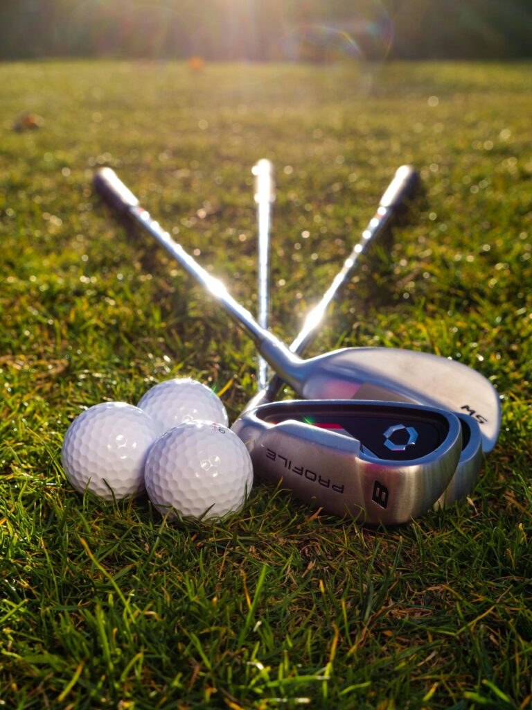 Golf clubs and balls arranged on a sunlit grass field, perfect sports imagery.